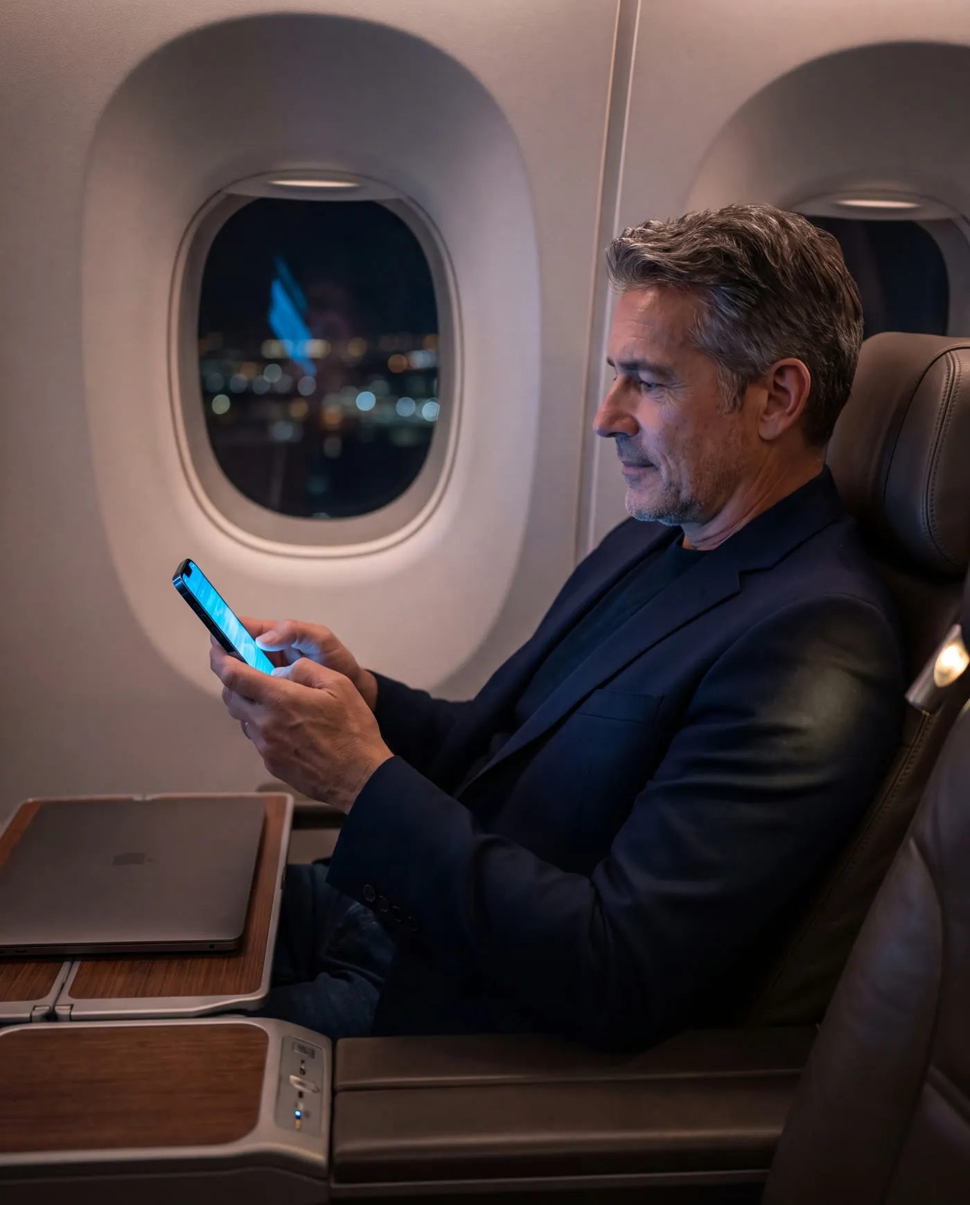 A senior executive typing a short message on his phone in a business class seat at night